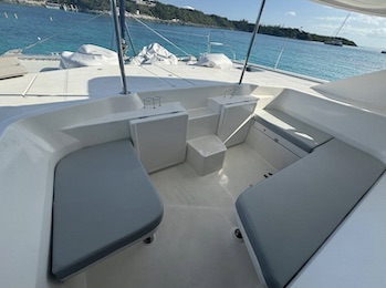The shaded aft cockpit of a catamaran, bench seating either side, looking out towards a moored boat