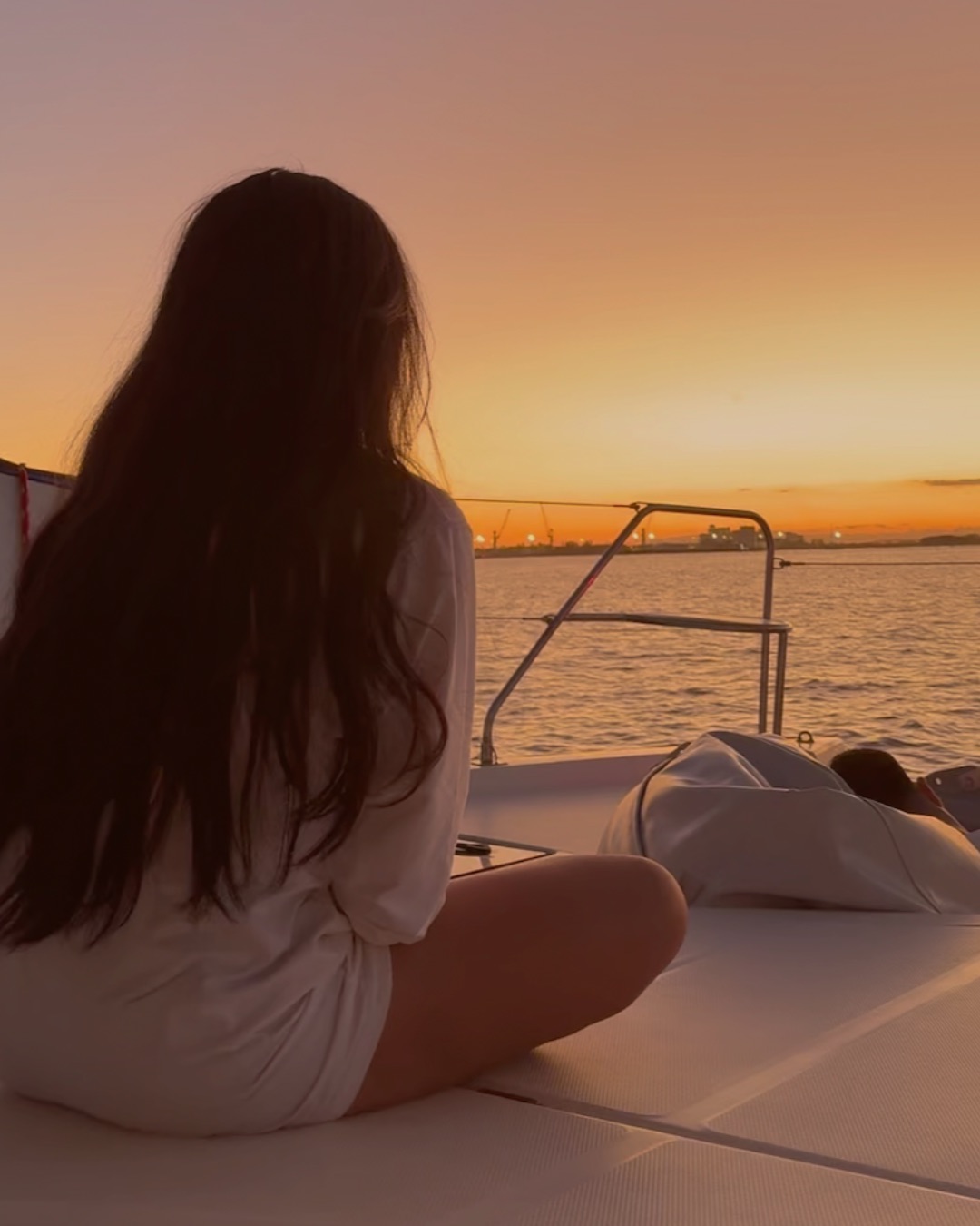 A guest sitting on the foredeck watching the sun set over the water from a boat at anchor