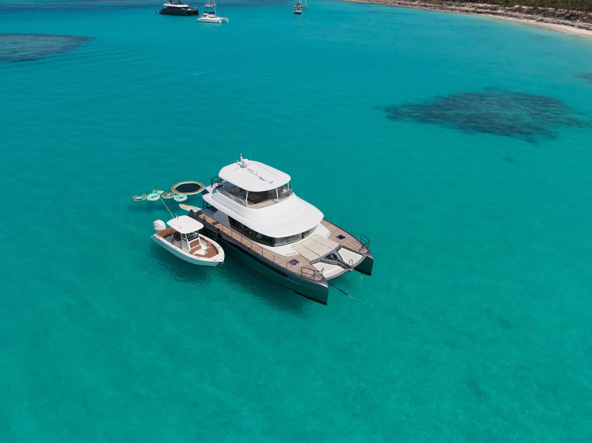 An aerial view of a power catamaran anchored in turquoise water, tender alongside and inflatables in the water